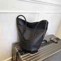 Minimalist black lychee leather bucket bag with silver chain on a silver suitcase - Black