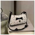 Détail du sac à nœud monochrome avec pendentif cœur doré posé sur un livre gris - Blanc