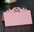 Pink laser-cut wedding place cards with heart bird design on a wooden background - Pink