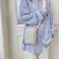 Detail of a beige nylon crossbody phone bag shown on a person for outdoor and daily use - White