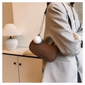 Detail view of brown quilted baguette bag with V-stitch texture and white fur ball charm - With Fur Pom-pom / Brown