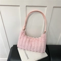 Close-up of pink faux fur shoulder bag with vertical quilted texture on a book - Pink