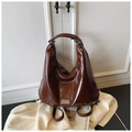 Detail of dark brown glossy leather Hobo bag with metal branding on white cloth - Coffee