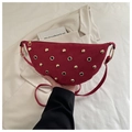 Detail shot of a red suede crescent bag with gold rivets and eyelet studs held by hand - Red