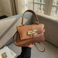 Brown lychee texture crossbody bag with gold twist lock on a minimalist grey sofa - Brown