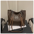 Close-up of a brown tote bag with M-pattern print and silver chain strap on a chair - Coffee