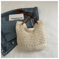 Close-up of cream woven tote bag featuring brown leather handles and metal rivet details - White