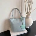 Minimalist mint green nylon handbag with heart pendant and slender handles on white books - Green