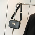 Black pleated crossbody bag with golden bow and wide fabric strap displayed on a hanger - Black