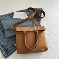 Brown faux suede tote bag with leather handles on a blue denim jacket background - Brown