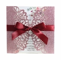 Close-up of laser-cut glitter pink wedding invitation with a deep red satin ribbon bow - Glitter Pink