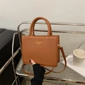 Brown PU leather square handbag with dual handles and adjustable strap on a metal shelf - Dark Brown