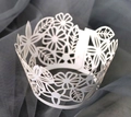Close-up of white laser-cut cupcake wrappers with delicate floral and leaf patterns - White
