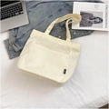 Dettaglio della borsa tote in tela crema con tasche anteriori ed etichetta tessile fashion - Bianco