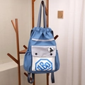 Sac à dos bleu à cordon avec base blanche et poche grise suspendu sur un cintre - Lettre Bleu Ciel