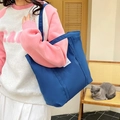 Detail of a navy blue canvas tote bag featuring a white side label and wide shoulder strap - Blue
