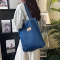 Gros plan d'un sac cabas en jean bleu foncé avec étiquette en cuir et bouton métal - Porté Main Bleu