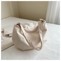 Detailed close-up of cream white tote bag with embossed fashion patch on a soft bed - White