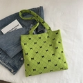 Green quilted tote bag with black bow patterns and corduroy texture on white bedding - Green