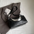 Bolso tote minimalista de cuero negro con detalle plateado sobre chaqueta marrón - Negro