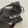 Bolso bandolera negro clásico con hebillas doradas sobre un elegante fondo de blazer gris - Negro