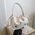Creamy white butterfly bucket bag featuring silver ornaments and drawstring closure - White