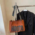 Braune Wildleder-Einkaufstasche mit HOOTO-Schriftzug und goldener Kette am Kleiderbügel - Kaffeebraun