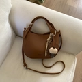 Detailed shot of brown lychee leather bucket bag with plush pom-pom charm on a white sofa - Yellow Brown (With Pendant)