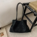 Detail of minimalist black oversized tote bag with soft pleated sides on a woven chair - PU Black Without Pendant