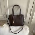 Detail of dark brown lychee leather bucket bag with vintage tassel charm on white sofa - Coffee (With Charm)
