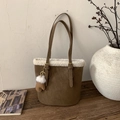 Brown suede bucket bag with white faux fur trim and glove charm on a wooden table - Brown