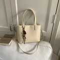 Close-up of cream leather bucket bag with beaded tassel charm on a white sofa - White (With Pendant)