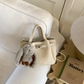 Detail van de crèmekleurige lederen emmertas met metalen sluiting en pluchen konijnenhanger - Beige Met Hanger