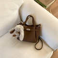 Detail van bruine handtas in generfd leer met zilveren slot en pluche konijnenhanger - Koffie met Hanger