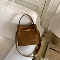 Primer plano de bolso saco de ante marrón con cierre dorado sobre mesa de madera minimalista - PU Marrón