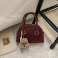 Detailaufnahme der dunkelroten Bowlingtasche mit Plüschwelpen-Anhänger auf Handtasche - Burgunderrot