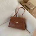 Detail of caramel brown lychee leather tote bag with silver rotary buckle on a cozy sofa - Brown