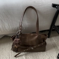 Detalle de bolso tote marrón oscuro con cinturón de ojales y colgante de bola a cuadros - Marrón con colgante