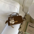 Detalle de bolso bandolera de ante marrón con un colgante de cachorro de peluche en un sofá - Gamuza Marrón