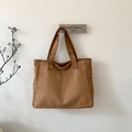 Detail view of dark brown suede tote bag with circular logo patch on white background - Brown