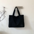 Detailed close-up of a large black matte tote bag hanging on a minimalist white wall - Black