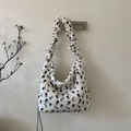 Dettaglio borsa trapuntata a pois con tracolla a pieghe e piccola etichetta arancione - Pois neri