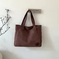 Detail view of dark brown suede tote bag with reinforced stitching and embossed logo patch - Brown