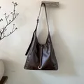 Detalle de bolso tote marrón oscuro con costuras en contraste y anillo metálico - café