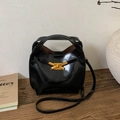 Dettaglio di una borsa a secchiello nera lucida con fibbia a fiocco dorata su tavolo in legno - Nero PU