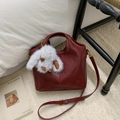 Detail view of burgundy leather bucket bag with white plush bunny charm and strap - With Charm / Burgundy