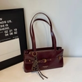 Detail of burgundy patent leather underarm bag with belt buckle and gold metal hardware - With Charm / Ankara Red