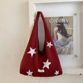 Detailed view of red plush tote bag with white star embroidery hanging on a textured wall - Red