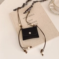 Mini black crossbody bag with beaded strap and silk scarf detail on a book surface - Black