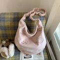 Detail view of pink velvet tote bag with bird embroidery and ruched strap on a sofa - Pink